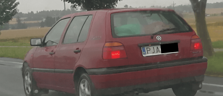 Dziecko leży za tylną szybą golfa. Kierowca jedzie starą drogą DK 11